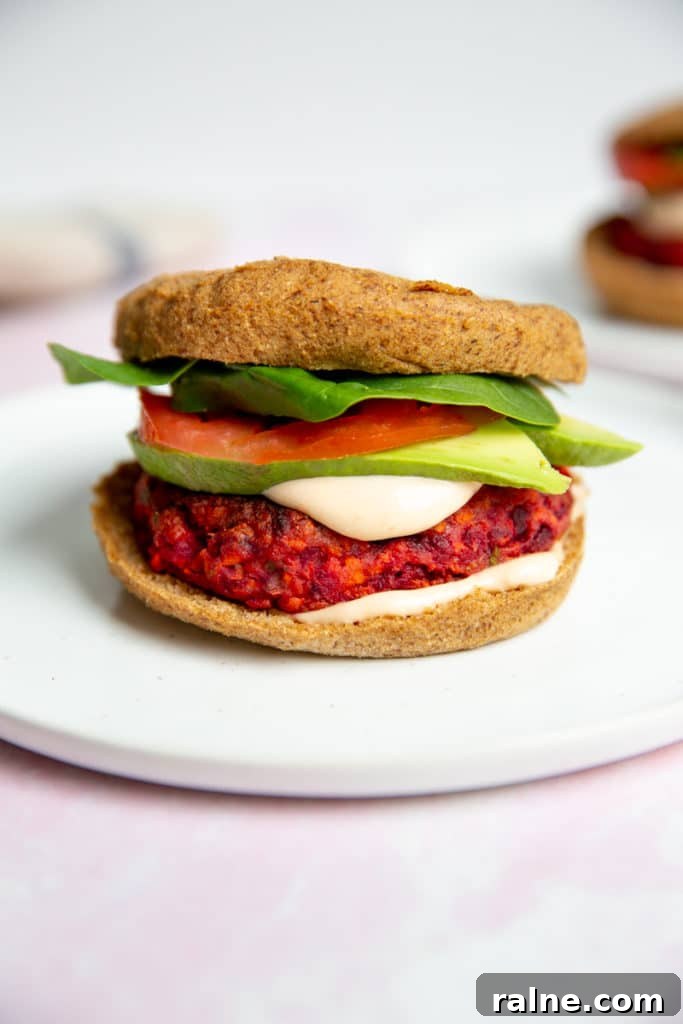 A gluten free veggie burger on a plate, topped with avocado, tomato and lettuce.