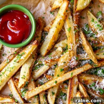 Baked french fries with herbs and parmesan on parchment paper with ketchup.