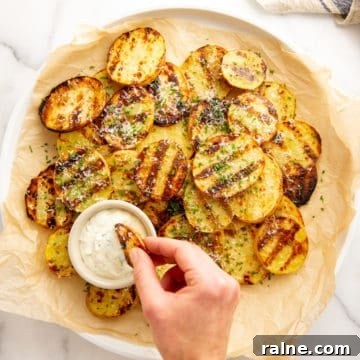 Grilled potatoes on a platter with a hand dipping one into a small bowl of aioli.