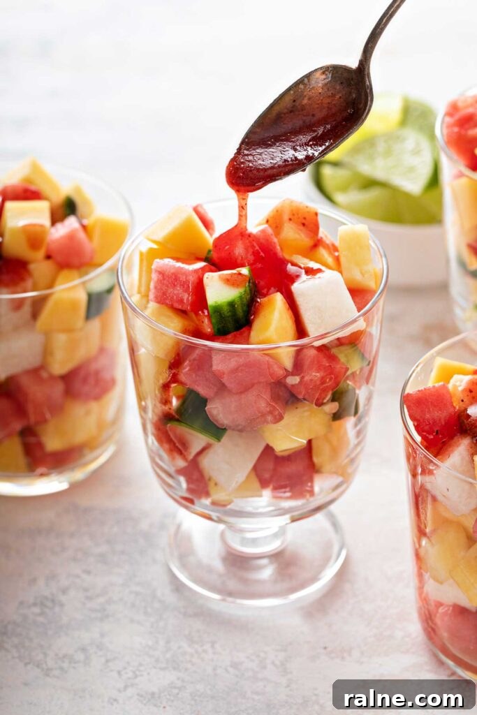 Authentic Mexican Fruit Cups (Vasos de Fruta) — Street Snack Recipe 6 A spoon drizzling chamoy sauce over fresh fruit pieces in a glass cup