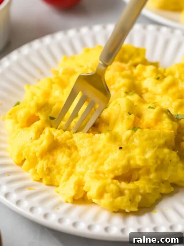 Hearty Breakfast Casserole Recipe for Busy Mornings 10 Fork diving into a pile of fluffy scrambled eggs on a white plate.