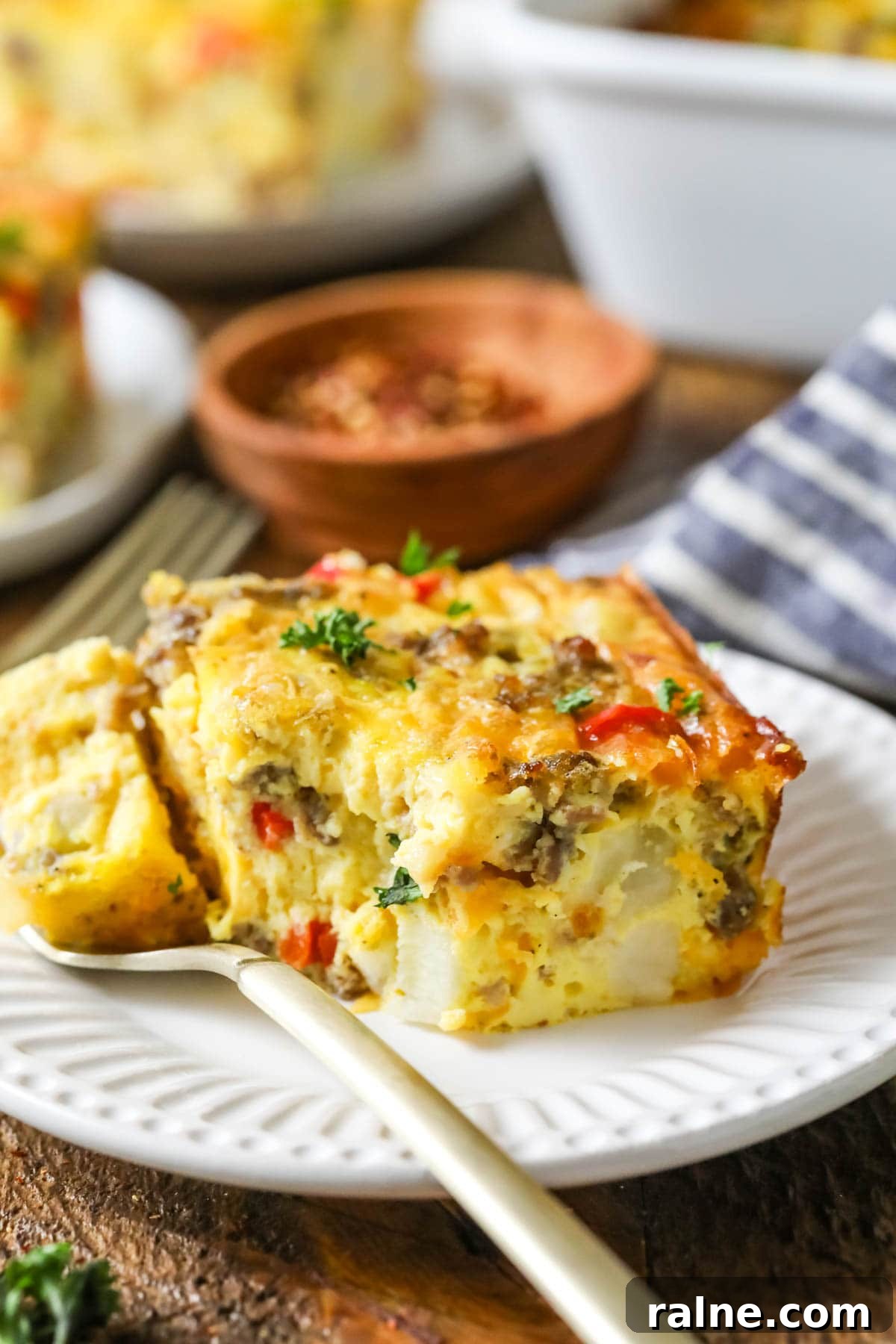 Hearty Breakfast Casserole Recipe for Busy Mornings 6 Fork taking a bite from a slice of casserole made with eggs, sausage, peppers, and more.
