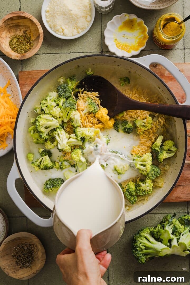 Creamy Broccoli Cheddar Orzo Bake with Parmesan Crust 5 Broccoli, orzo, and milk being added to a braiser pot to make broccoli cheddar orzo.