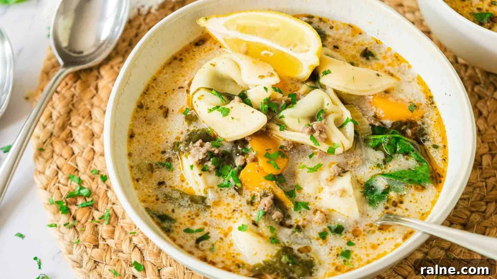 17 Comforting Soup Recipes for Quiet Evenings 17 A bowl of creamy tortellini soup with spinach, lemon wedges, and herbs, served with a spoon.