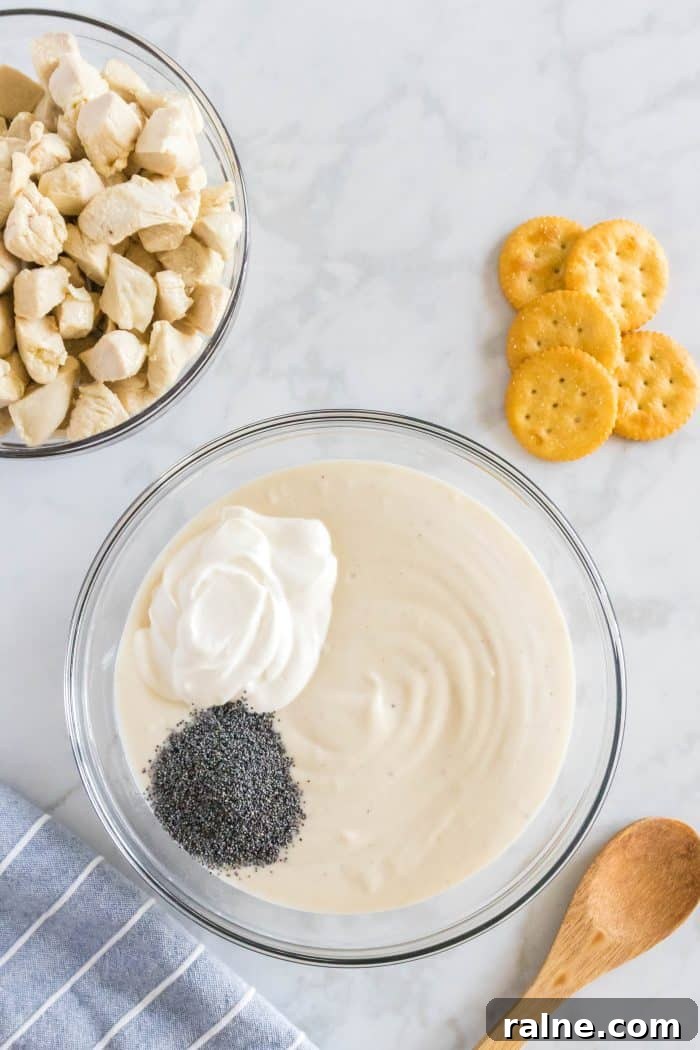 Creamy Poppy Seed Chicken Casserole with Ritz Topping 4 Sour cream and poppy seeds added to a large glass mixing bowl filled with canned cream of chicken soup.