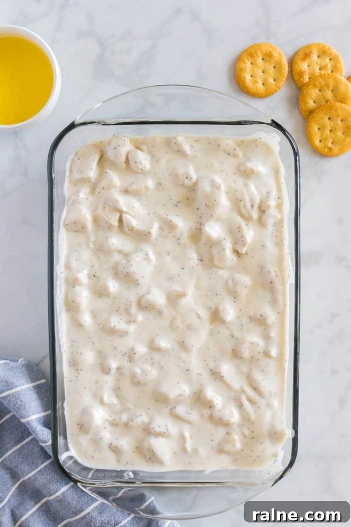 Creamy Poppy Seed Chicken Casserole with Ritz Topping 6 Glass baking dish filled completely with cooked chicken pieces coated completely in a mixture of canned cream of chicken soup with poppy seeds and sour cream.