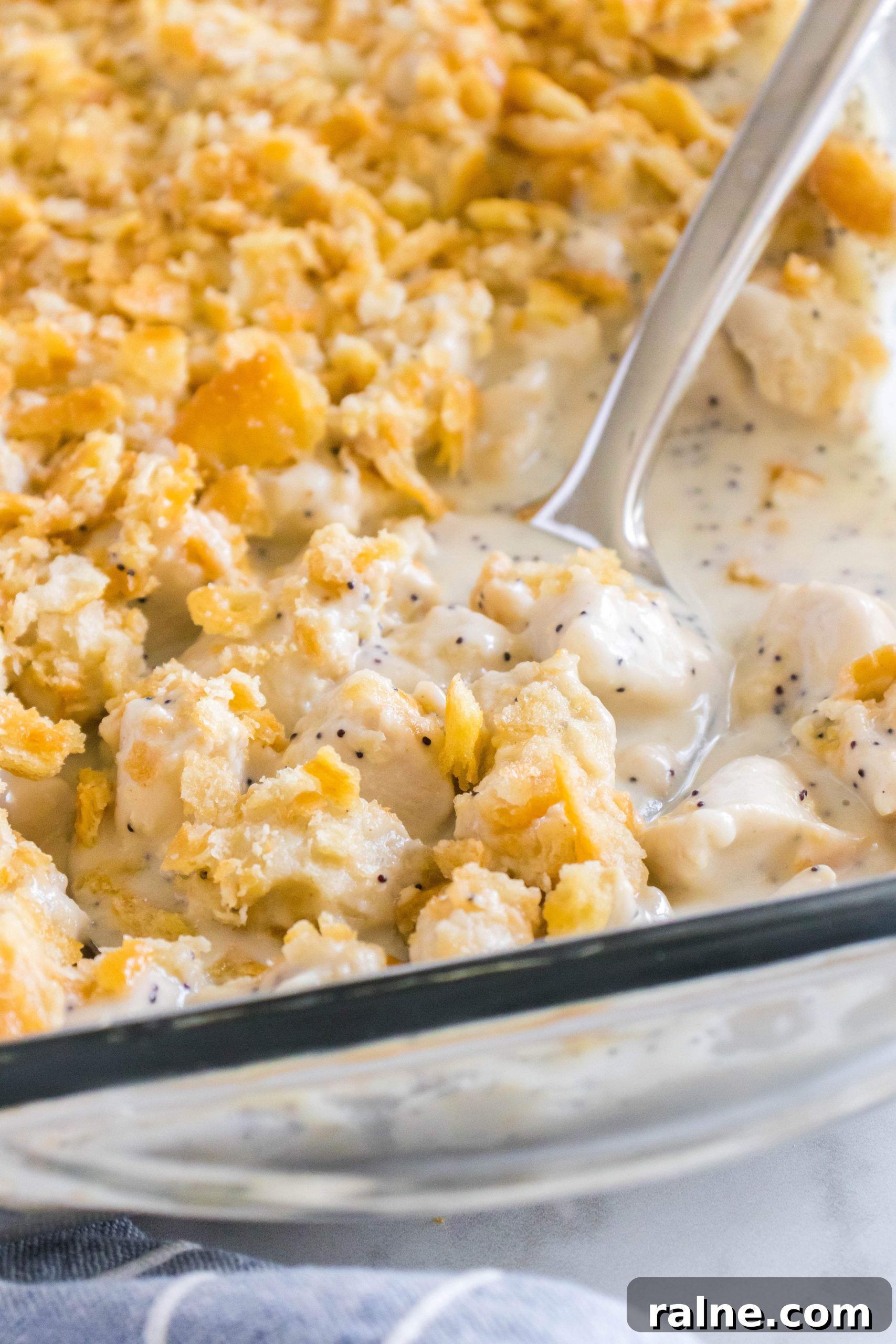 Creamy Poppy Seed Chicken Casserole with Ritz Topping 8 Large serving spoon resting in a glass baking dish filled with poppy seed chicken casserole.