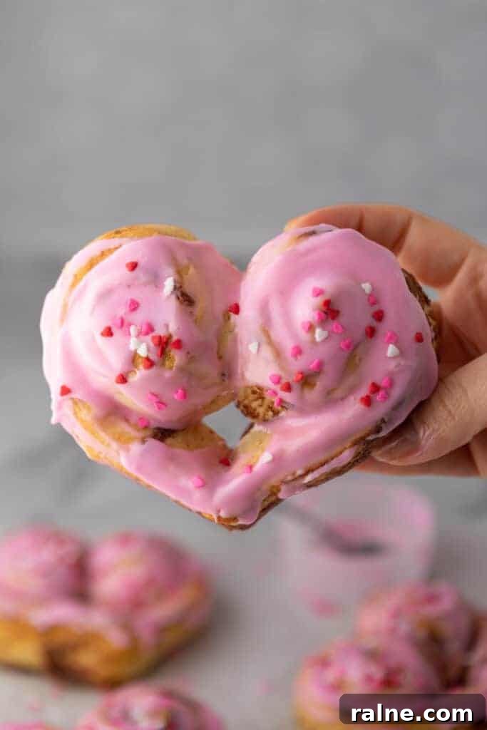 Heart-shaped cinnamon roll with pink frosting and Valentine’s sprinkles held in hand