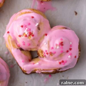 Frosted heart-shaped cinnamon rolls with pink icing and Valentine’s sprinkles