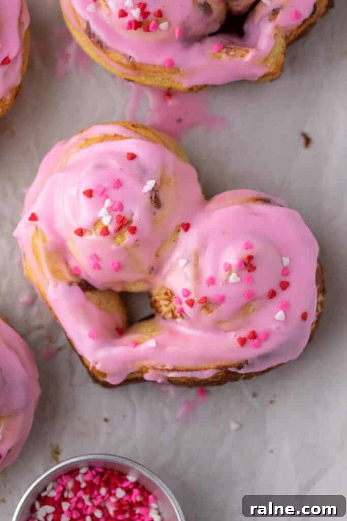 Frosted heart-shaped cinnamon rolls with pink icing and Valentine’s sprinkles
