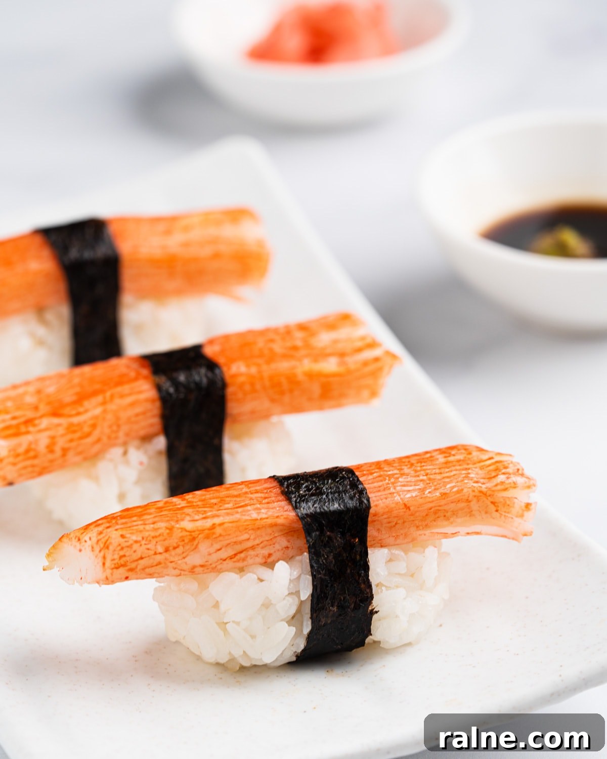 Kanikama sushi on a white plate with a side of soy sauce, wasabi and pickled ginger.