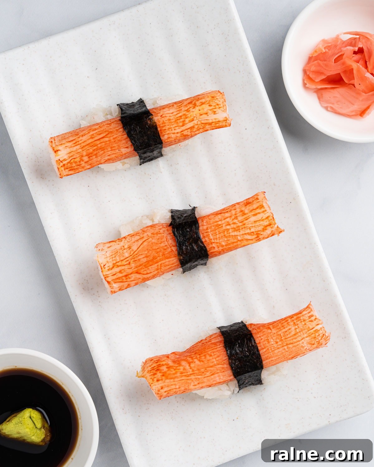 top down view of Kanikama nigiri sushi on a white plate with a side of soy sauce, wasabi and pickled ginger.