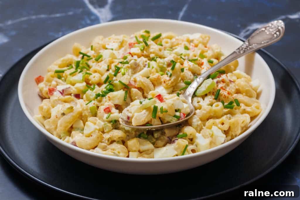 23 Make-Ahead Salads That Stay Fresh in the Fridge and Lunch Bag 25 A bowl of Deviled Egg Pasta Salad with chopped vegetables and herbs, is set on a black plate, and a spoon rests in it.