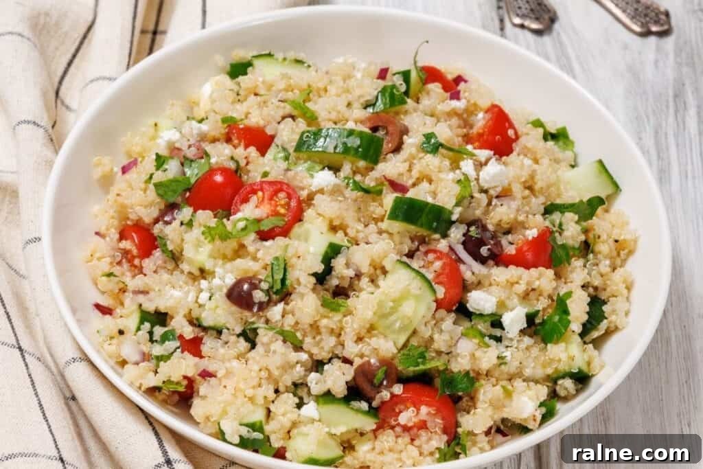 23 Make-Ahead Salads That Stay Fresh in the Fridge and Lunch Bag 5 A bowl of Easy Mediterranean Quinoa Salad on a wooden surface with a striped cloth nearby.