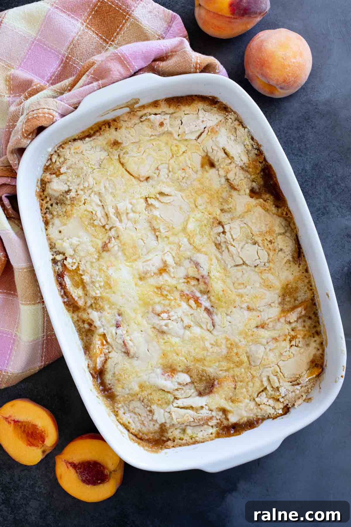 Baking dish with peach dump cake, with fresh peaches on the side.