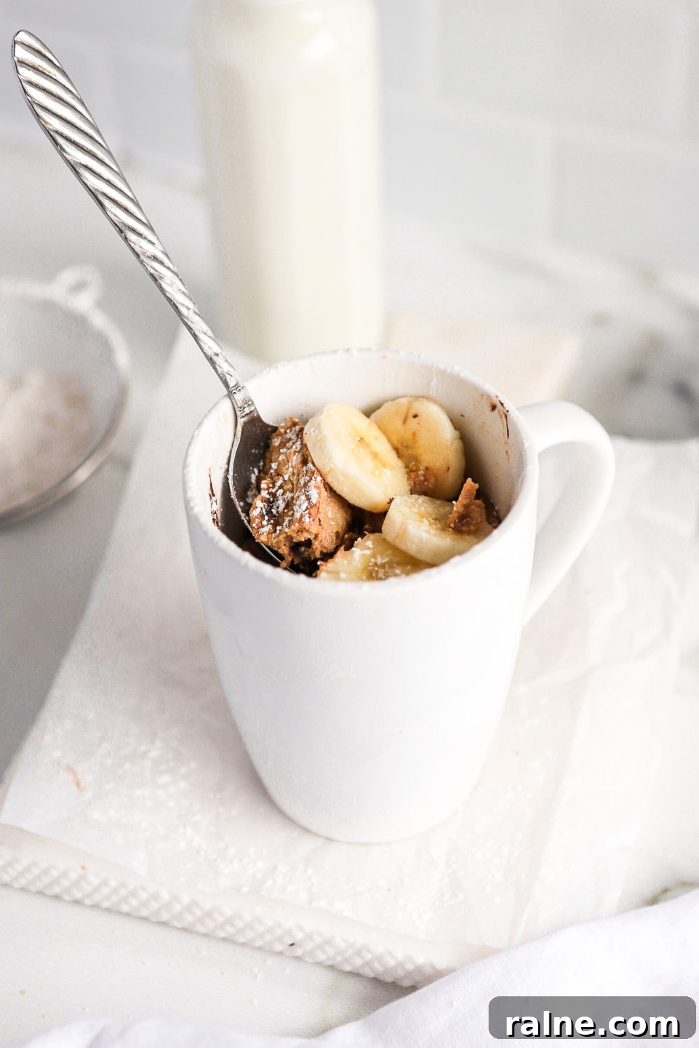 Gluten-Free Banana Bread Mug Cake Recipe (Quick Single-Serve) 6 high protein banana mug cake topped with banana slices with a silver spoon