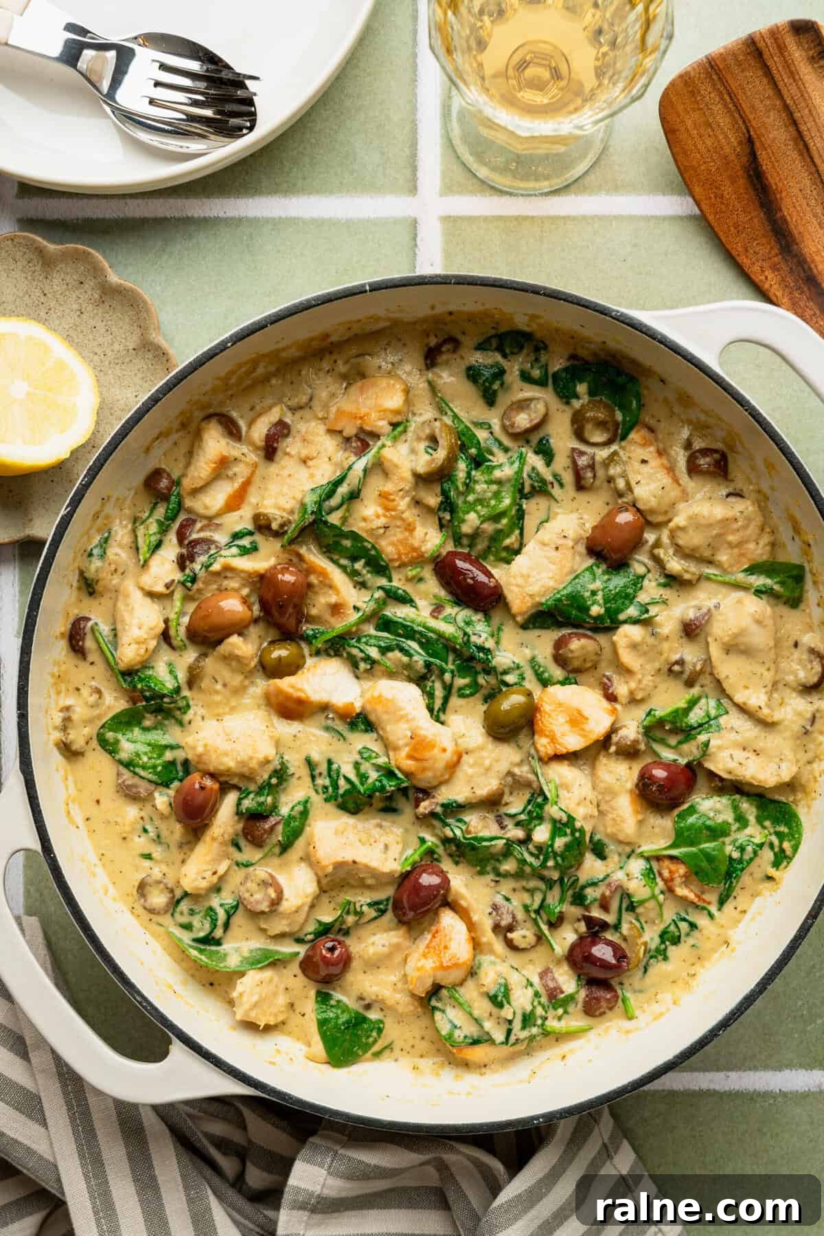 A pan with a creamy chicken Alfredo in it topped with spinach and black olives.