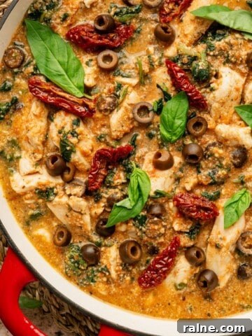 A pan with a cooked chicken dish in it in a red creamy sauce topped with fresh basil and chopped black olives.
