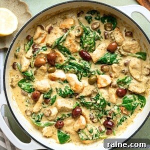 A pan filled with a creamy chicken Alfredo topped with spinach and chopped black olives.
