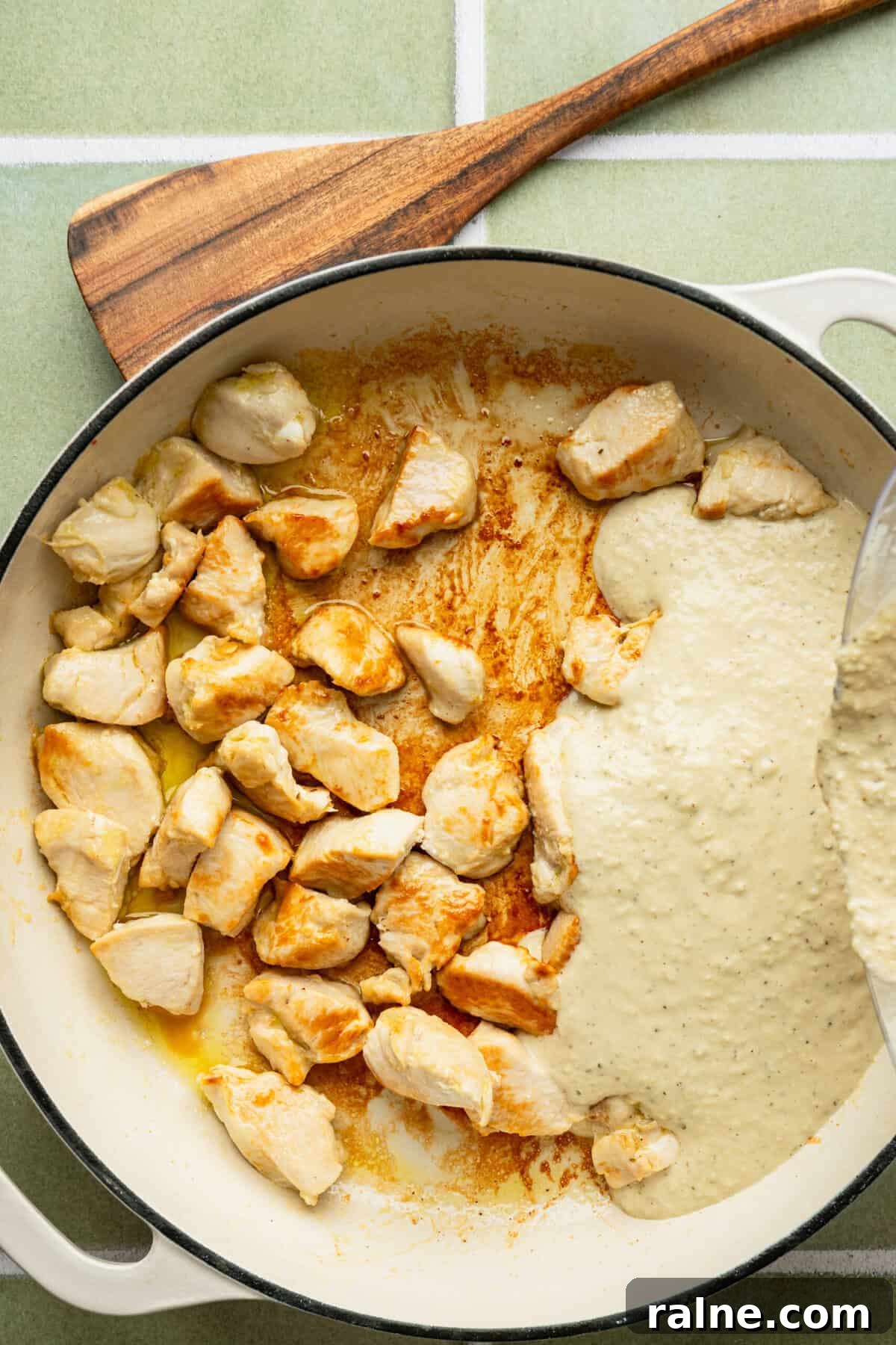 A pan filled with cooked chicken pieces with a white sauce being poured over them.