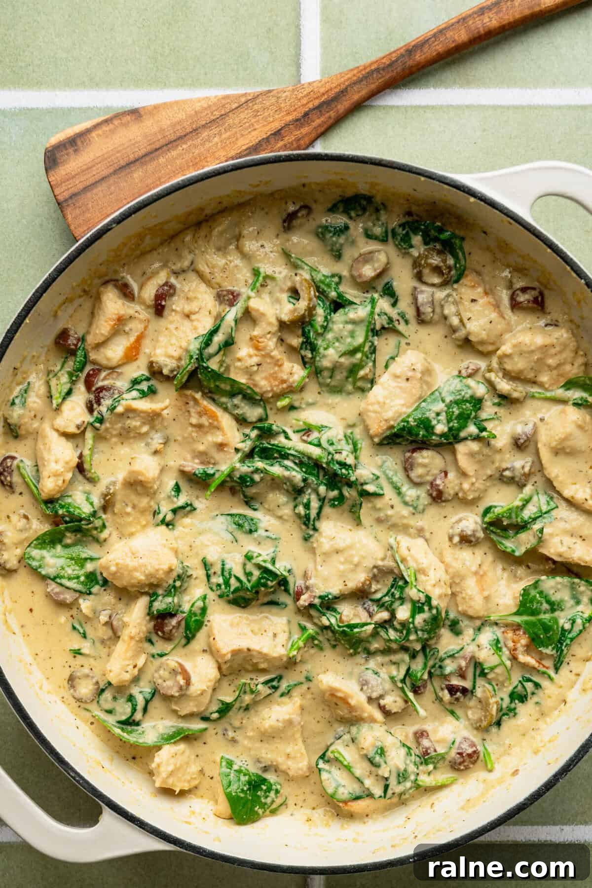 A pan filled with a creamy chicken Alfredo sauce with spinach and chopped black olives mixed in.
