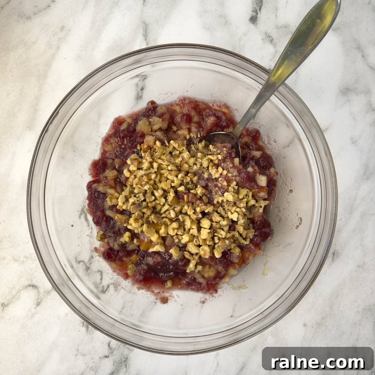 Fruit for a cranberry salad combined with chopped walnuts in a glass bowl.