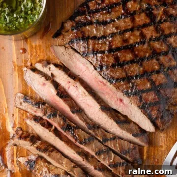 Partially sliced flank steak with perfect grill marks on a brown wood board.