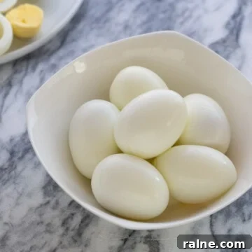A small white bowl of peeled hard boiled eggs.