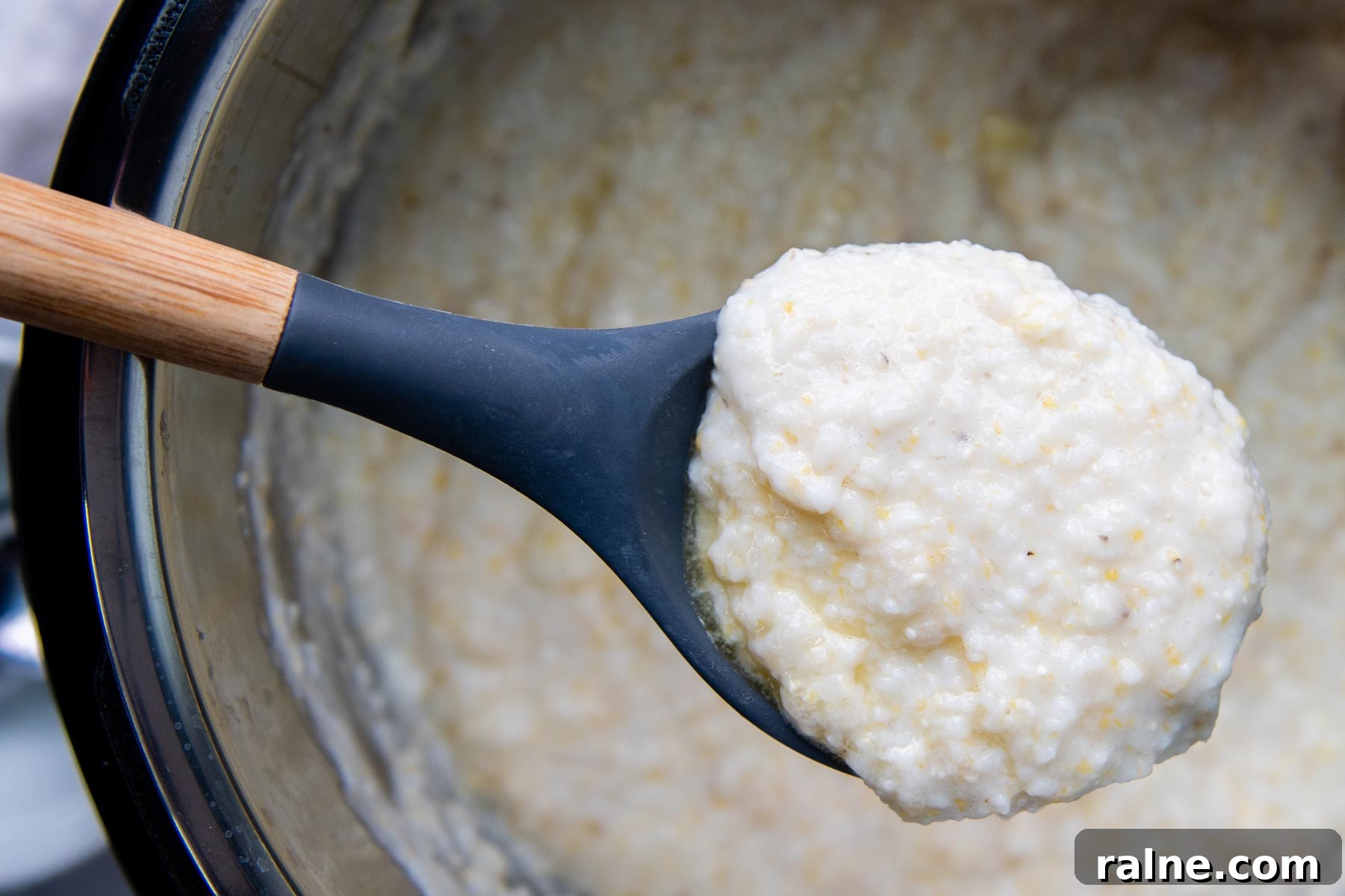 a ladle holding up creamy grits from a pot.