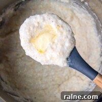 a scoop of grits with melted butter on top being held up from an instant pot.