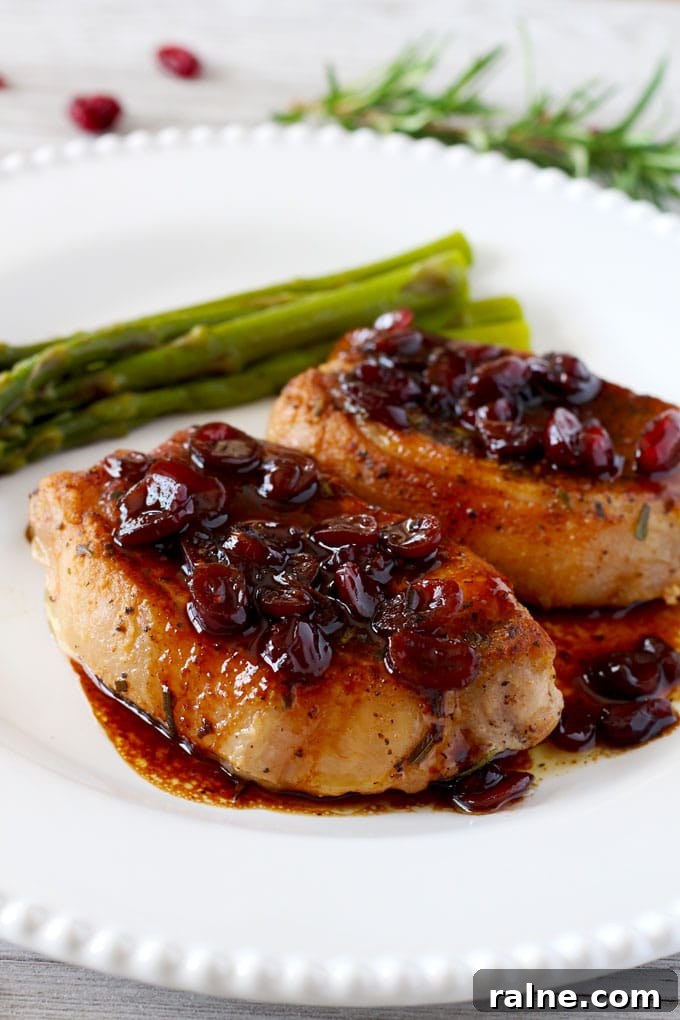 Two boneless pork chops with port and cranberries served on a white plate.